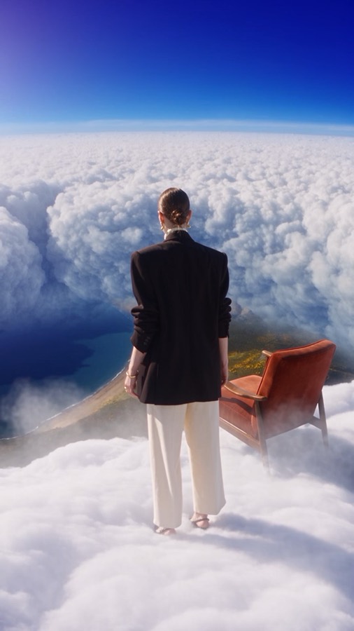 Above the Clouds ad: a woman in a black blazer standing on clouds beside a leather armchair